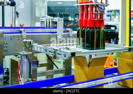 A robot arm is loading glass bottles into boxes on an automated industrial machine on a production line. Stock Photo