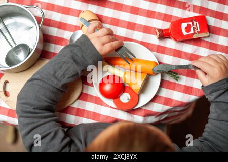 Top view of child's hands playing at cooking with wooden food. Cutlery, plates, pot. Stock Photo