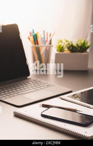 A modern home office desk featuring a laptop, notebook, smartphone, pen, and office supplies. Perfect setup for remote work or studying - Bright and o Stock Photo