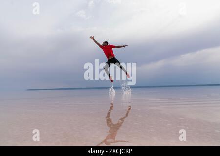 A man is jumping into the air in the sea. Happy young man jumping in the air on the beach at sunset Stock Photo
