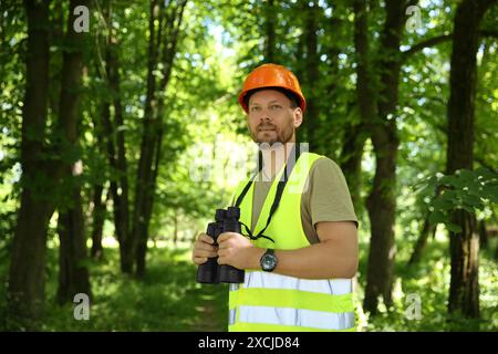 Forester with binoculars examining plants in forest Stock Photo