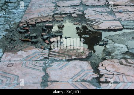 Damaged or broken sidewalk tiles, causing stagnant water. Stock Photo