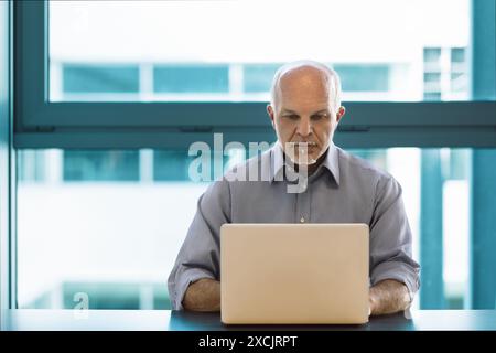 Senior man works on a laptop in a modern office, focused and confident, using the latest technology to stay productive Stock Photo