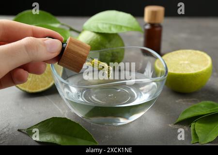 Woman dripping essential oil from pipette into bowl at gray table, closeup Stock Photo