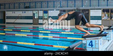 Professional female swimmer preparing and jumping off the starting block into the pool. Competitive swimmers workout concept. Stock Photo