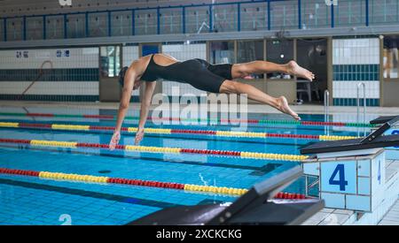 Professional female swimmer preparing and jumping off the starting block into the pool. Competitive swimmers workout concept. Stock Photo