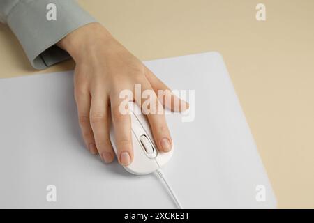 Woman using modern wired computer mouse on beige background, closeup Stock Photo