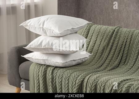 Stack of soft white pillows on sofa and blanket indoors Stock Photo