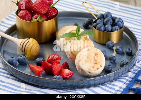 Round small fried cheesecakes on a blue plate with berries. Healthy breakfast Stock Photo