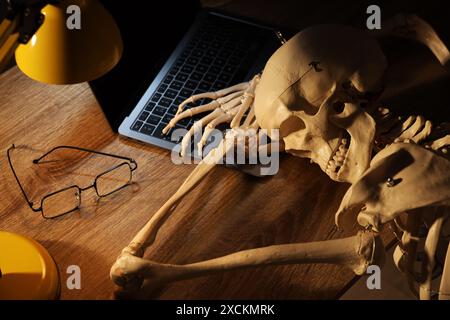 Waiting concept. Human skeleton sleeping at wooden table with laptop Stock Photo