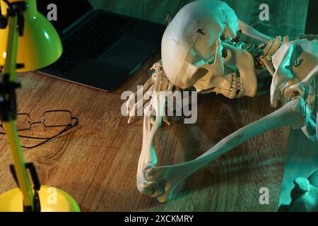 Waiting concept. Human skeleton sleeping at wooden table with laptop Stock Photo