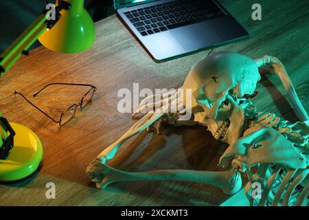 Waiting concept. Human skeleton sleeping at wooden table with laptop Stock Photo