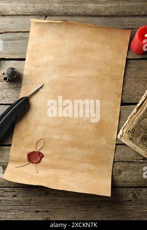 Sheet of old parchment paper with wax stamp, black feather, inkwell, vintage book and candle on wooden table, flat lay Stock Photo