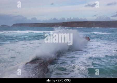 Waves crashing over Sennen Cove's Jetty; stormy seas in Cornwall Stock Photo