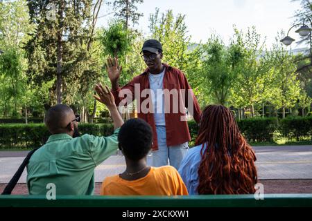 Pleasant meeting of calm relaxed African American students friends in park, sitting on alley bench Stock Photo