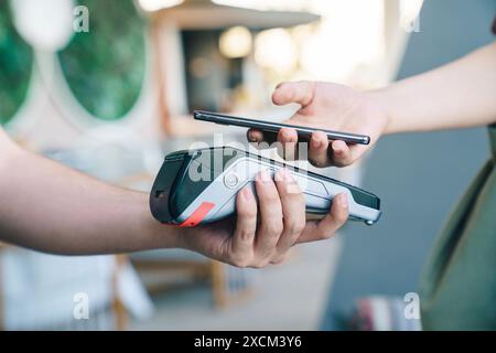 woman paying bill through smartphone using NFC technology in a restaurant. Stock Photo