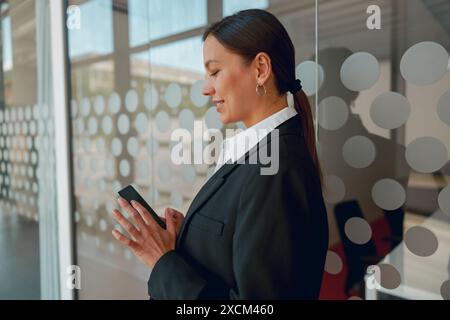 A businesswoman in a modern office uses a smartphone to stay connected and productive Stock Photo