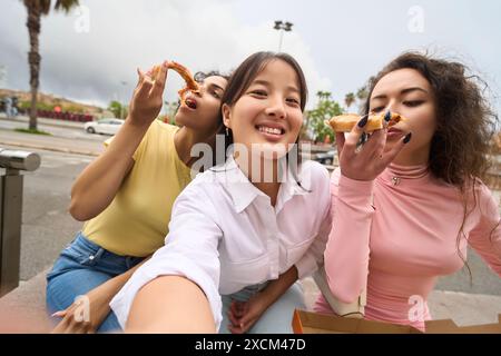 Three women are eating pizza and smiling Stock Photo
