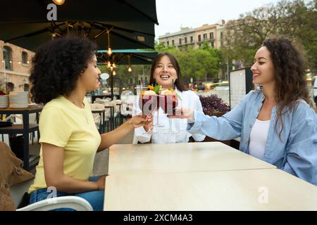 Three women are sitting at a table, laughing and holding up their wine glasses Stock Photo