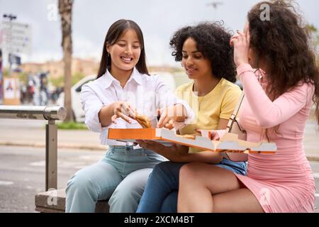 Three young multiethnic women sharing pizza outdoors Stock Photo