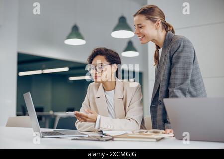 Two busy female coworkers discussing project while working in office and use laptop Stock Photo