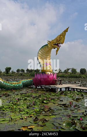 Close-up of a giant Naga sculpture rising out of a lotus from a wetland pond, surrounded by lilypads, Thailand Stock Photo