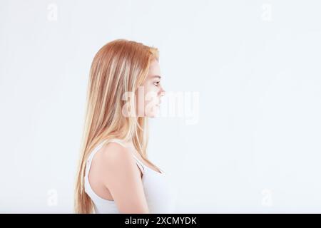 Portrait of a young woman with long blonde hair standing against a white background, showing a neutral facial expression Stock Photo