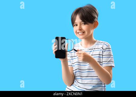 Little boy with mobile phone and magnifier on blue background Stock Photo