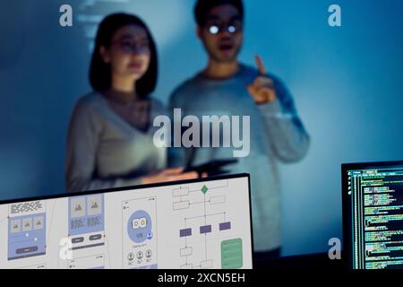 UX designer works on a tablet while a colleague tests  application in the background in office Stock Photo