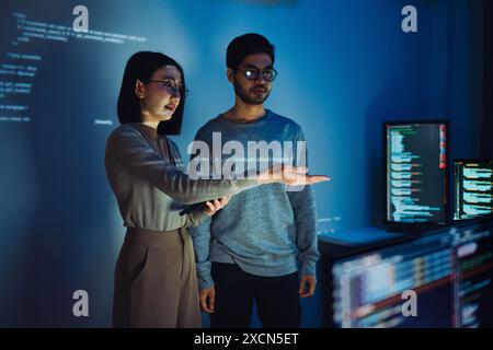 Asian Two software developers engaged in collaborative coding session, with code projected onto the wall and multiple computer screens displaying Stock Photo