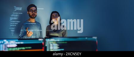 Asian Two software developers engaged in collaborative coding session, with code projected onto the wall and multiple computer screens displaying Stock Photo