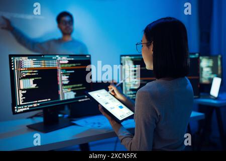 UX designer works on a tablet while a colleague tests  application in the background in office Stock Photo