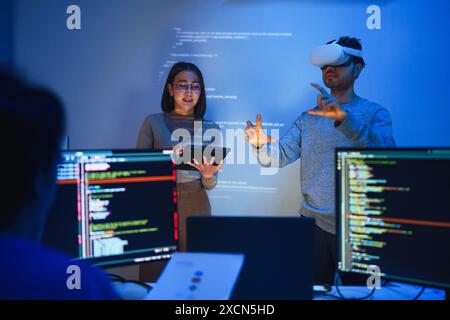 developer uses a VR headset to interact with projected interface designs, while colleagues discuss and code on screens, highlighting the integration o Stock Photo