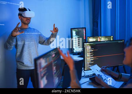 developer uses a VR headset to interact with projected interface designs, while colleagues discuss and code on screens, highlighting the integration o Stock Photo