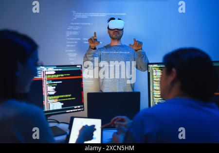 developer uses a VR headset to interact with projected interface designs, while colleagues discuss and code on screens, highlighting the integration o Stock Photo