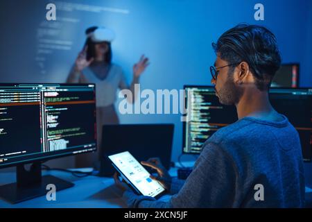 developer uses a VR headset to interact with projected interface designs, while colleagues discuss and code on screens, highlighting the integration o Stock Photo