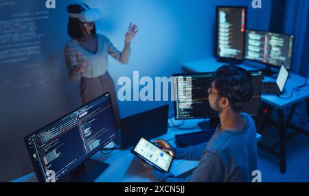 developer uses a VR headset to interact with projected interface designs, while colleagues discuss and code on screens, highlighting the integration o Stock Photo