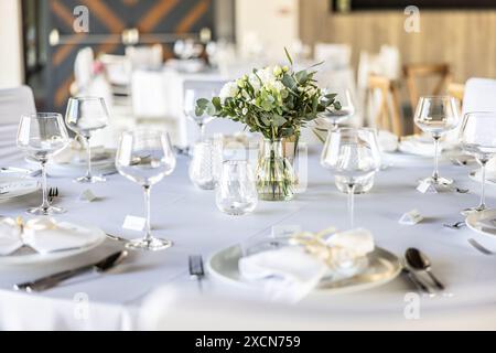 A wedding table covered with a white tablecloth, decorated with flowers, candles, glasses and cutlery. Stock Photo