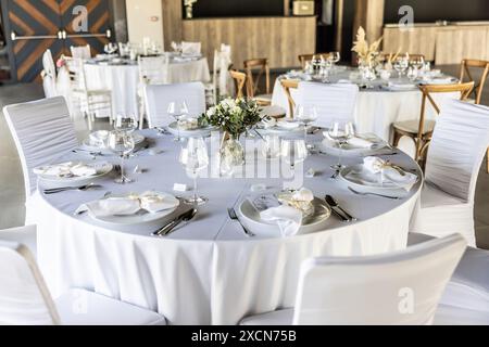 A wedding table covered with a white tablecloth, decorated with flowers, candles, glasses and cutlery. Stock Photo