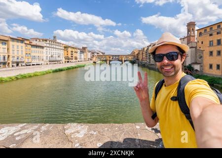 Young man enjoys beautiful view on famous Old bridge in Florence, sitting back on the riverside at sunset. man traveler visiting italian landmarks. tr Stock Photo