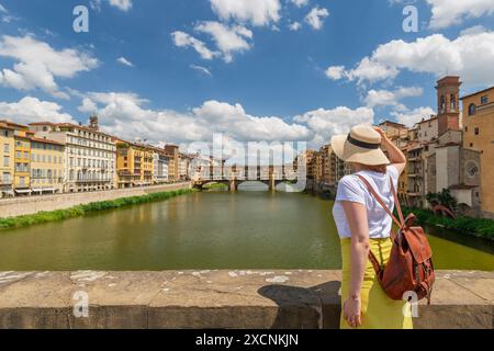 Young woman enjoys beautiful view on famous Old bridge in Florence, standing back on the riverside at sunset. Female traveler visiting italian landmar Stock Photo