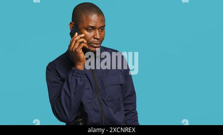Portrait of security guard at work using phone to make call to friends while overseeing premises. Private law enforcement worker in telephone call with mates, studio backdrop, camera A Stock Photo