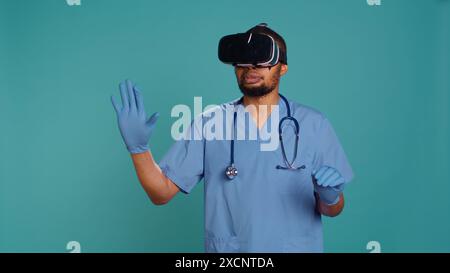 African american doctor wearing virtual reality goggles, remotely operating patient. Hospital staff member using high tech medical vr device, isolated over studio backdrop, camera B Stock Photo