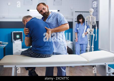 Osteopathic nurse gently extends spine of elderly patient with injury as part of physiotherapy. Chiropractor provides aid to gentleman experiencing back pains, aiding in physical recovery. Stock Photo