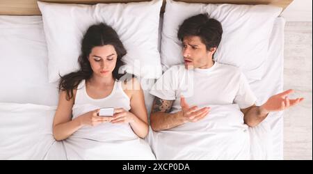 Man Complaining To Woman On Phone In Bed Stock Photo