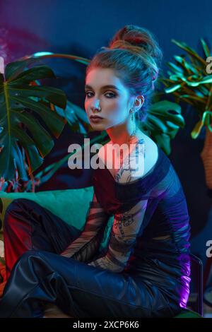 Young woman, wearing a black sheer dress, poses with tropical plants in front of a blue and red neon light Stock Photo