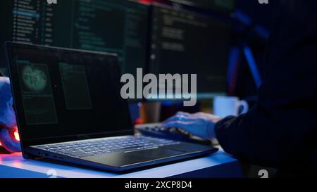 Hooded script kiddie taking laptop out of suitcase, prepared to launch DDoS attack. Close up shot of scammer at computer desk getting notebook from bag, starting work on malware script, camera B Stock Photo