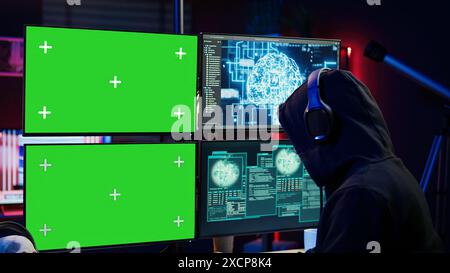 Hacker using isolated screen monitor and artificial intelligence to write spyware software, listening music. Scammer wearing headphones using AI and chroma key PC to do fraud using AI, camera B Stock Photo