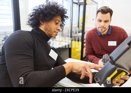 Two engineers engaged in programming a robotic system with a gripper arm, focusing on industrial automation and robotics training in a workshop settin Stock Photo