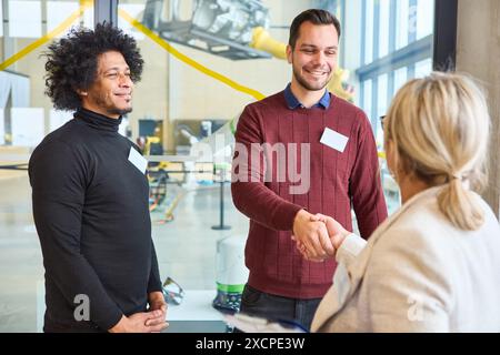 Two men are seen welcoming a woman with a handshake at a robotics training session, suggesting a professional and collaborative environment. Stock Photo